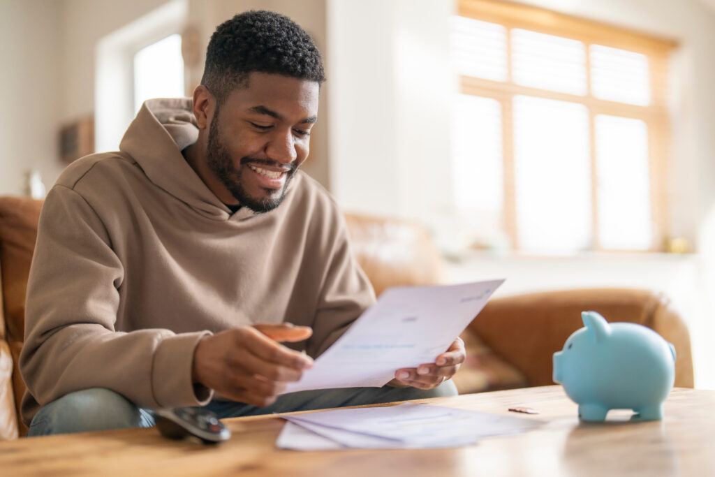 Person sitting at a table smiling while reviewing a document, with a piggy bank nearby