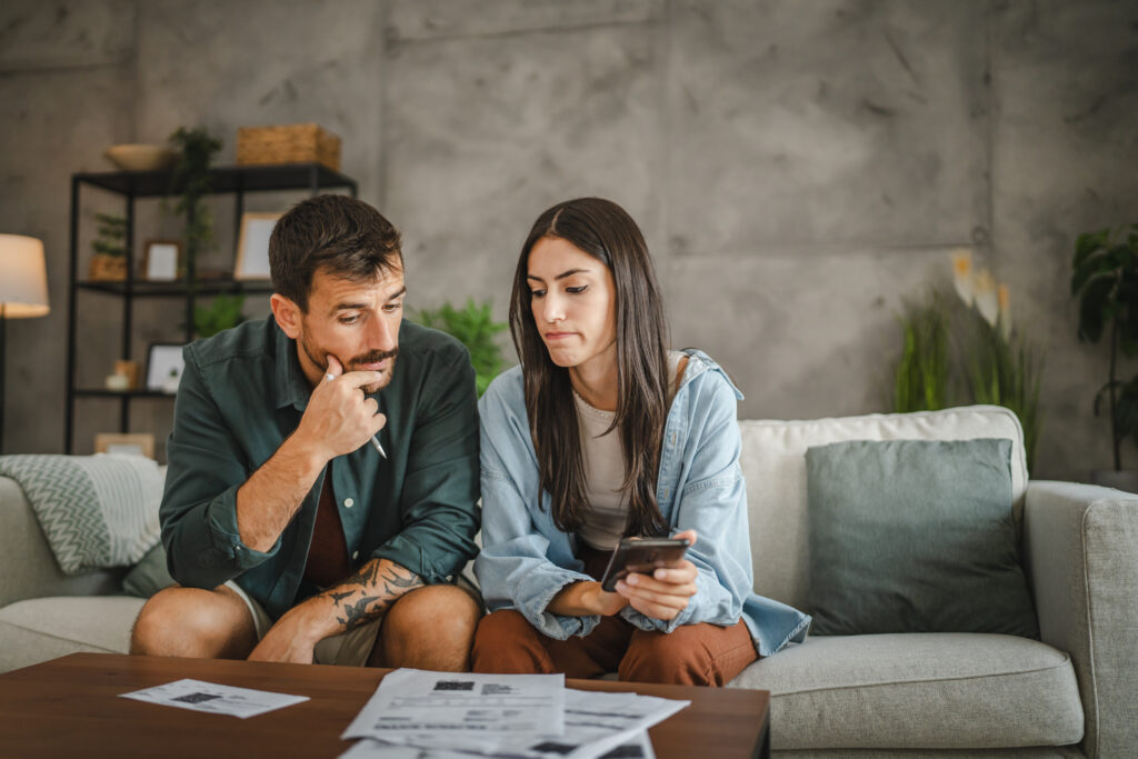 Two adults looking at financial documents together at home, checking information on a smartphone.