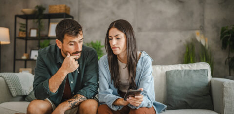 Two adults looking at financial documents together at home, checking information on a smartphone.