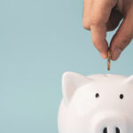 Hand putting coin to white piggy bank saving on blue background