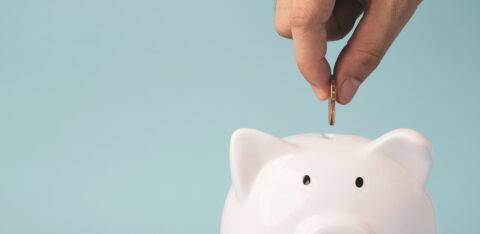 Hand putting coin to white piggy bank saving on blue background