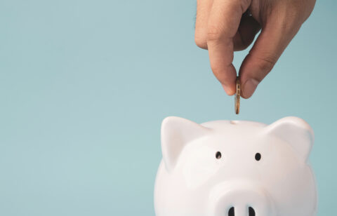 Hand putting coin to white piggy bank saving on blue background
