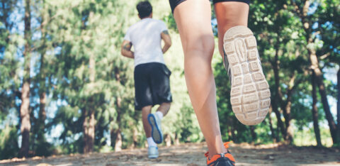 Close-up of two people running on a dirt trail, with focus on legs and shoes in motion