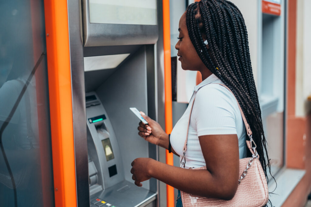 APerson using an ATM, holding a card while standing in front of the machine