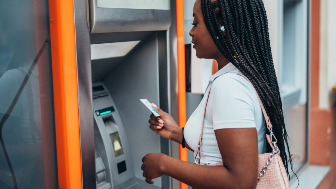 APerson using an ATM, holding a card while standing in front of the machine