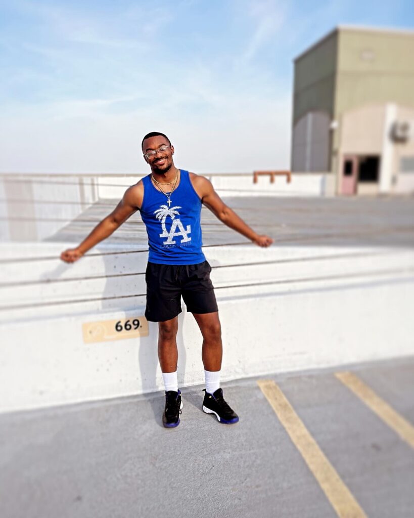 Man standing on a rooftop parking area, smiling and leaning back against a concrete barrier